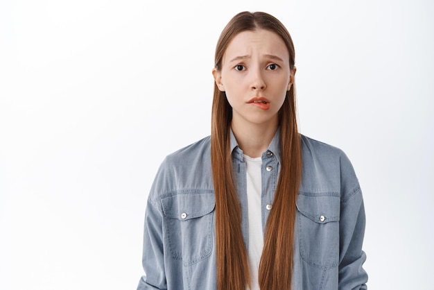 Concerned and worried teenage student girl biting lip and frowning looking nervous feeling scared or anxious standing troubled against white background