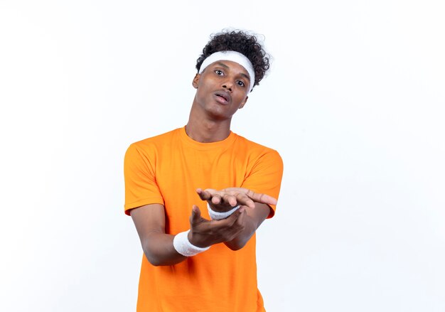 concerned young afro-american sporty man wearing headband and wristband holding out hands