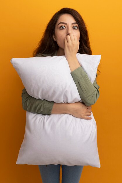 Concerned young beautiful girl wearing olive green t-shirt hugged pillow bites nails isolated on yellow wall