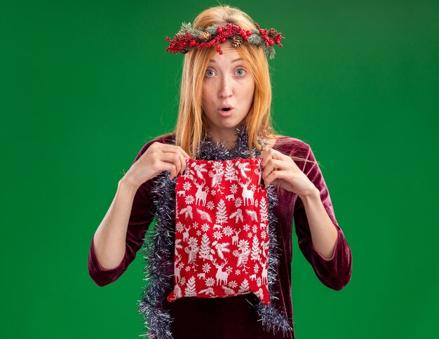 녹색 배경에 고립 된 크리스마스 가방을 들고 목에 화 환과 갈 랜드와 빨간 드레스를 입고 우려 젊은 아름 다운 소녀