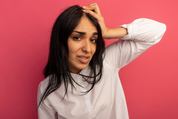 Concerned young beautiful girl wearing white t-shirt grabbed head isolated on pink