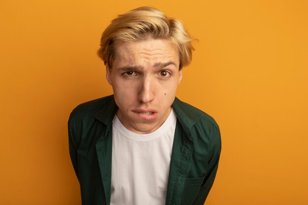 Concerned young blonde guy wearing green t-shirt bites lip