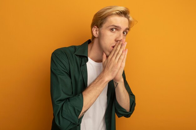 Concerned young blonde guy wearing green t-shirt covered face with hand