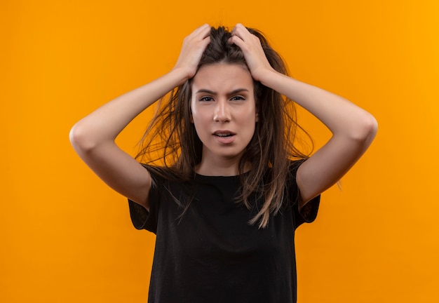 Concerned young caucasian girl wearing black t-shirt grabbed hair on isolated orange wall