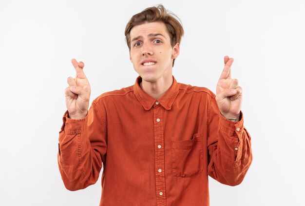 Concerned young handsome guy wearing red shirt crossing fingers 