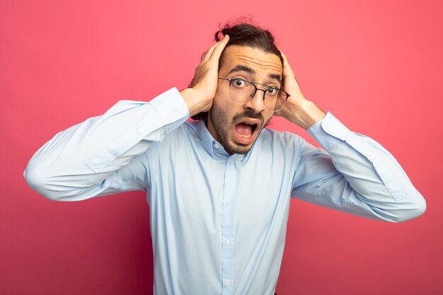 Concerned young handsome man wearing glasses keeping hands on head looking at front isolated on pink wall