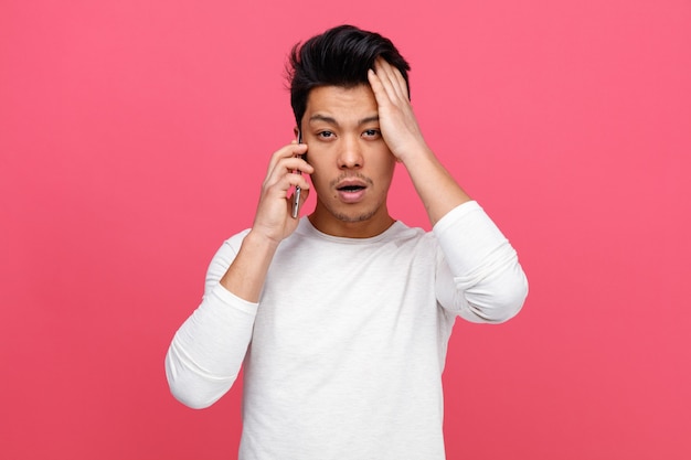 Concerned young man talking on phone keeping hand on head 