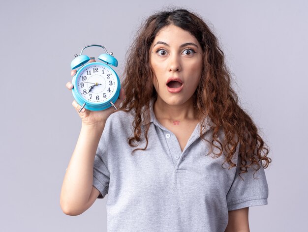 Concerned young pretty caucasian girl holding alarm clock  isolated on white wall