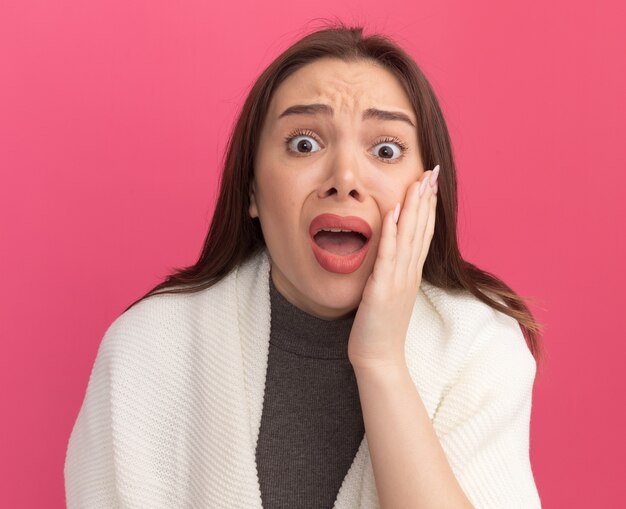 Concerned young pretty woman keeping hand on cheek  isolated on pink wall