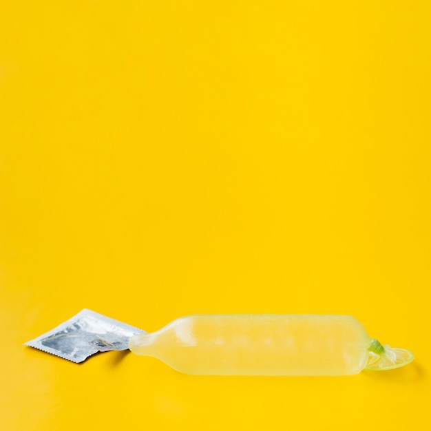 Condom filled with water and wrapper on yellow background