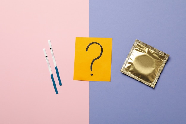 Condom, question mark and pregnancy tests on two tone surface