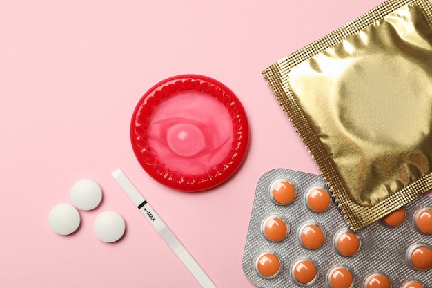 Condoms and pills on pink surface