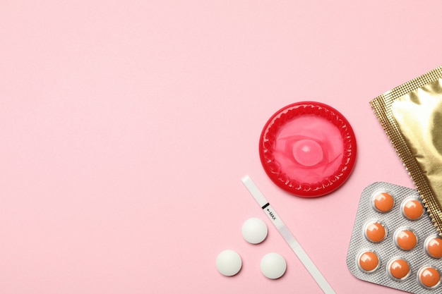 Condoms and pills on pink wall, space for text