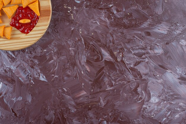 Cone chips with ketchup in a wooden plate , on the marble table. 