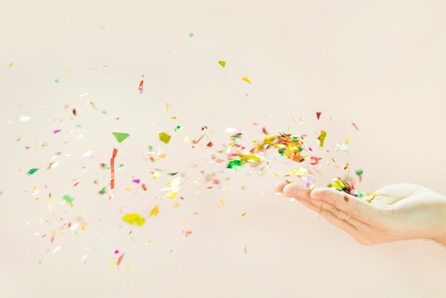 Confetti blowing from hands against beige background