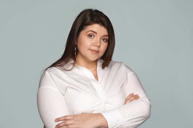 Confidence, business, people and lifestyle concept. Confident young overweight female with chubby cheeks and natural make up posing with arms crossed on her chest, expressing reluctance