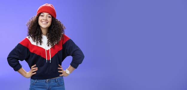 Confident ad energized cute european woman with curly hairstyle in warm beanie and stylish sweatshir