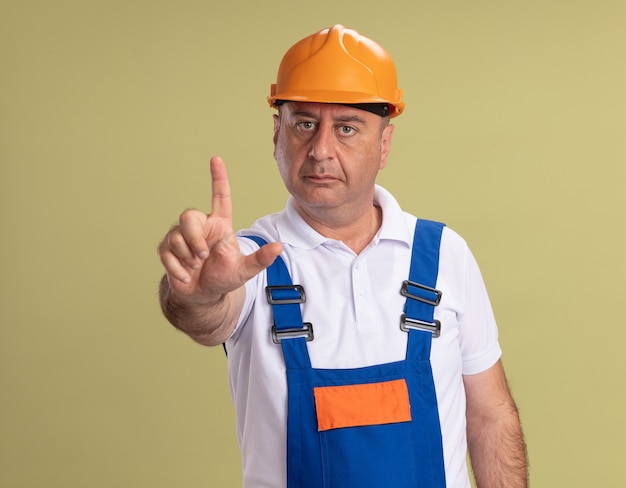 Confident adult builder man points up isolated on olive green wall