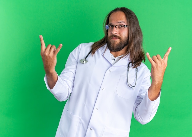 Уверенный взрослый мужчина-врач в медицинском халате и стетоскоп в очках делает рок-знак