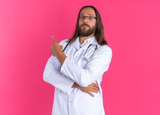 Confident adult male doctor wearing medical robe and stethoscope with glasses pointing up 