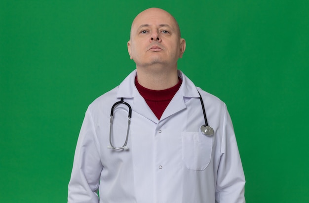 Uomo adulto sicuro in uniforme del medico con lo stetoscopio che guarda in su