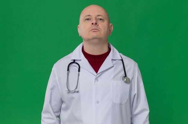 Уверенный взрослый мужчина в униформе врача со стетоскопом, глядя вверх