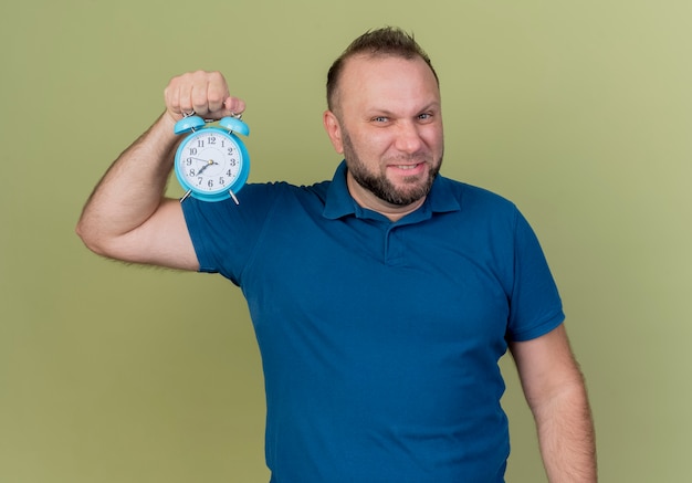 Confident adult slavic man holding alarm clock looking 