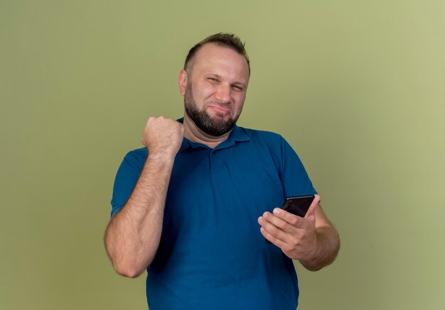 Confident adult slavic man holding mobile phone and clenching fist 