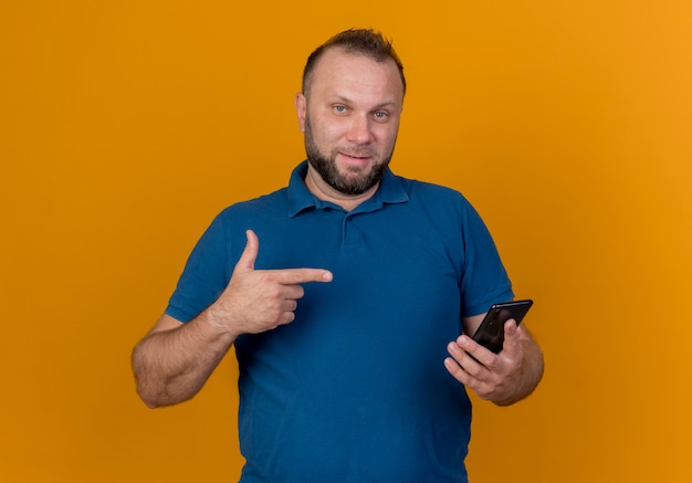 Confident adult slavic man holding and pointing at mobile phone looking 