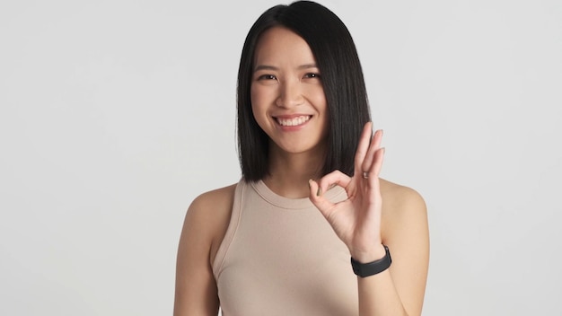 Confident Asian girl showing okay gesture smiling at camera over white background Asian woman posing isolated Like it