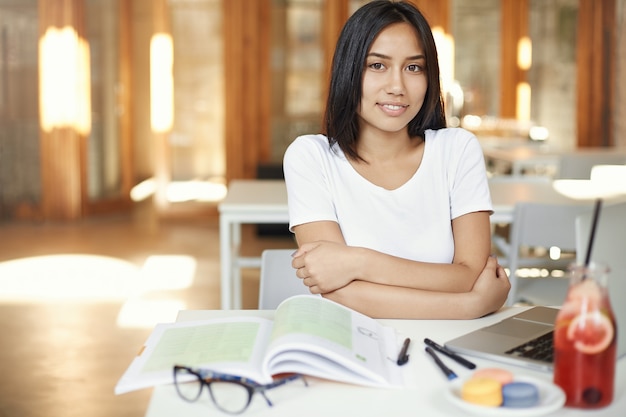 Уверенная азиатская студентка, работающая в библиотеке или коворкинге, готовится к экзаменам.