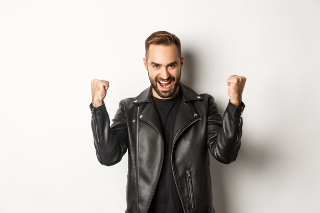 Confident and assertive man in leather jacket making fist pump, rejoicing of winning, feeling encouraged and satisfied 