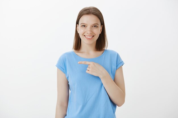 Confident and assertive smiling woman inviting check out event, pointing finger left