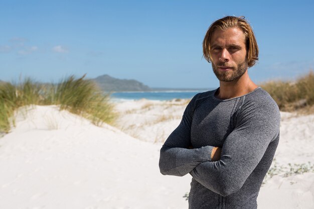 Confident athlete standing at beach against sky