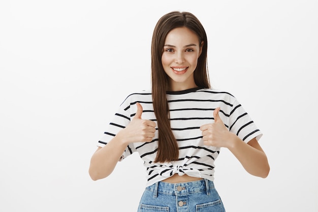 Confident attractive girl showing thumbs-up, well done gesture, compliment good choice