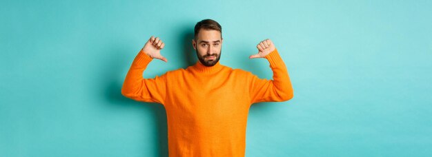 Confident attractive guy pointing at himself showoff or brag standing over light blue background