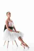 Free photo confident ballet dancer sitting on chair with crossed leg against white backdrop