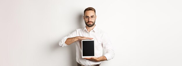 Free photo confident bearded man showing digital tablet screen demonstrating app standing over white background