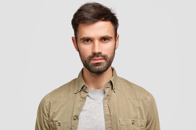 confident bearded man with dark hair, has serious facial expression, thinks about future job, dressed in fashionable shirt
