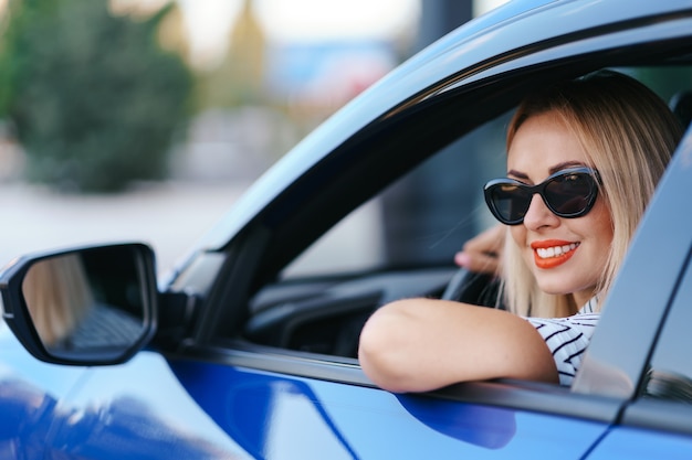 Donna sicura e bella in occhiali da sole. vista posteriore della giovane femmina attraente in abbigliamento casual alla guida di un'auto