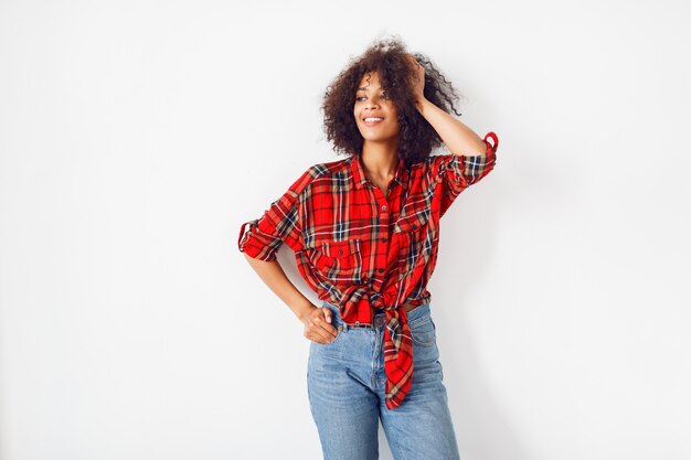 Confident black girl posing over white background. Wearing red  checkered shirt. Blue jeans.