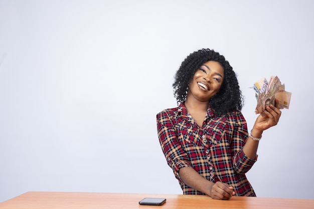 Confident black lady sitting and holding a wad of cash on an isolated background