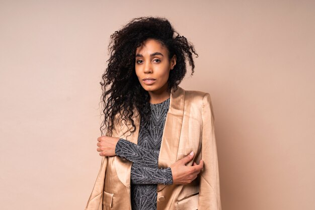 Confident black woman in golden silk jacket and shiny dress with perfect tan body posing.