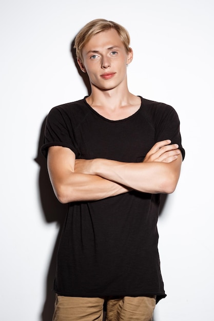 Confident blond handsome young man wearing black t-shirt with hands crossed on chest