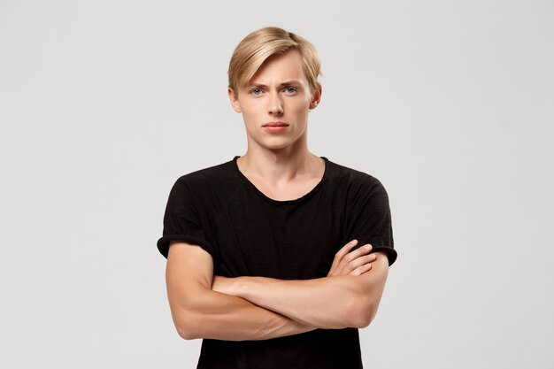 confident blond handsome young man wearing black t-shirt with hands crossed on chest