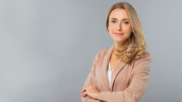 Confident blonde young businesswoman standing against gray background