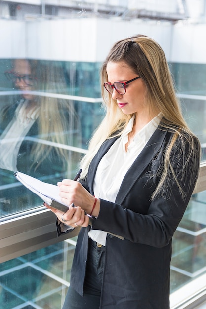 Confident blonde young woman writing in the document with pen