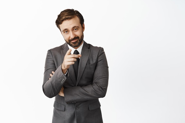 Confident boss company ceo in suit pointing finger at camera with pleased face we need you recruiting for job standing over white background