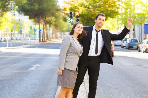 Confident business colleagues catching cab and standing on road