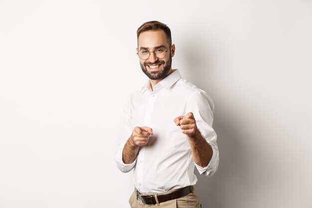 Confident businessman smiling, pointing fingers at you, congrats or praise gesture, standing  